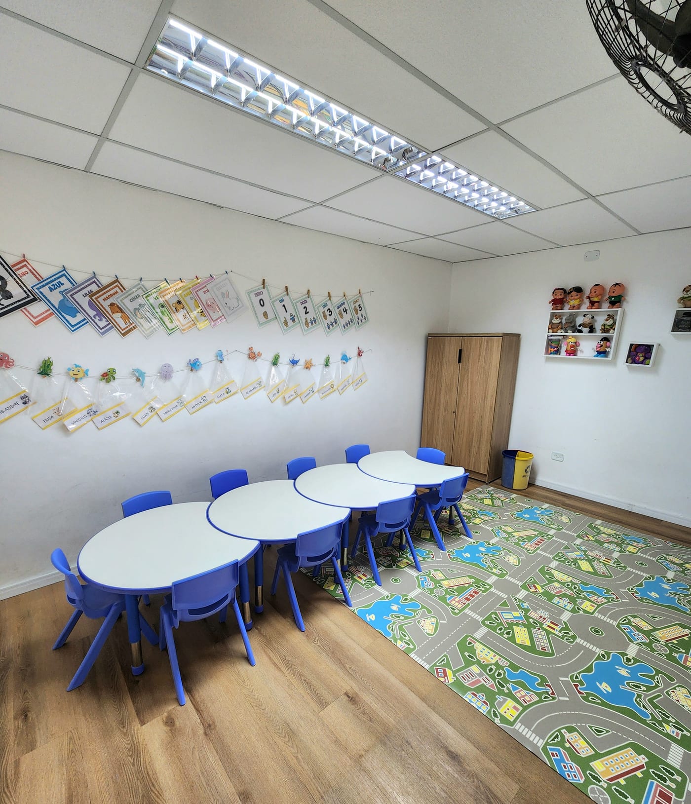 Ambiente de aprendizagem com mesas, cadeiras azuis e tapete ilustrado