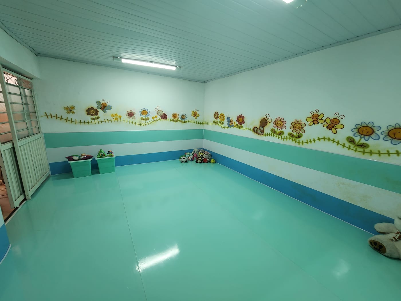 Área de recreação com piso azul esverdeado e paredes decoradas com bichinhos