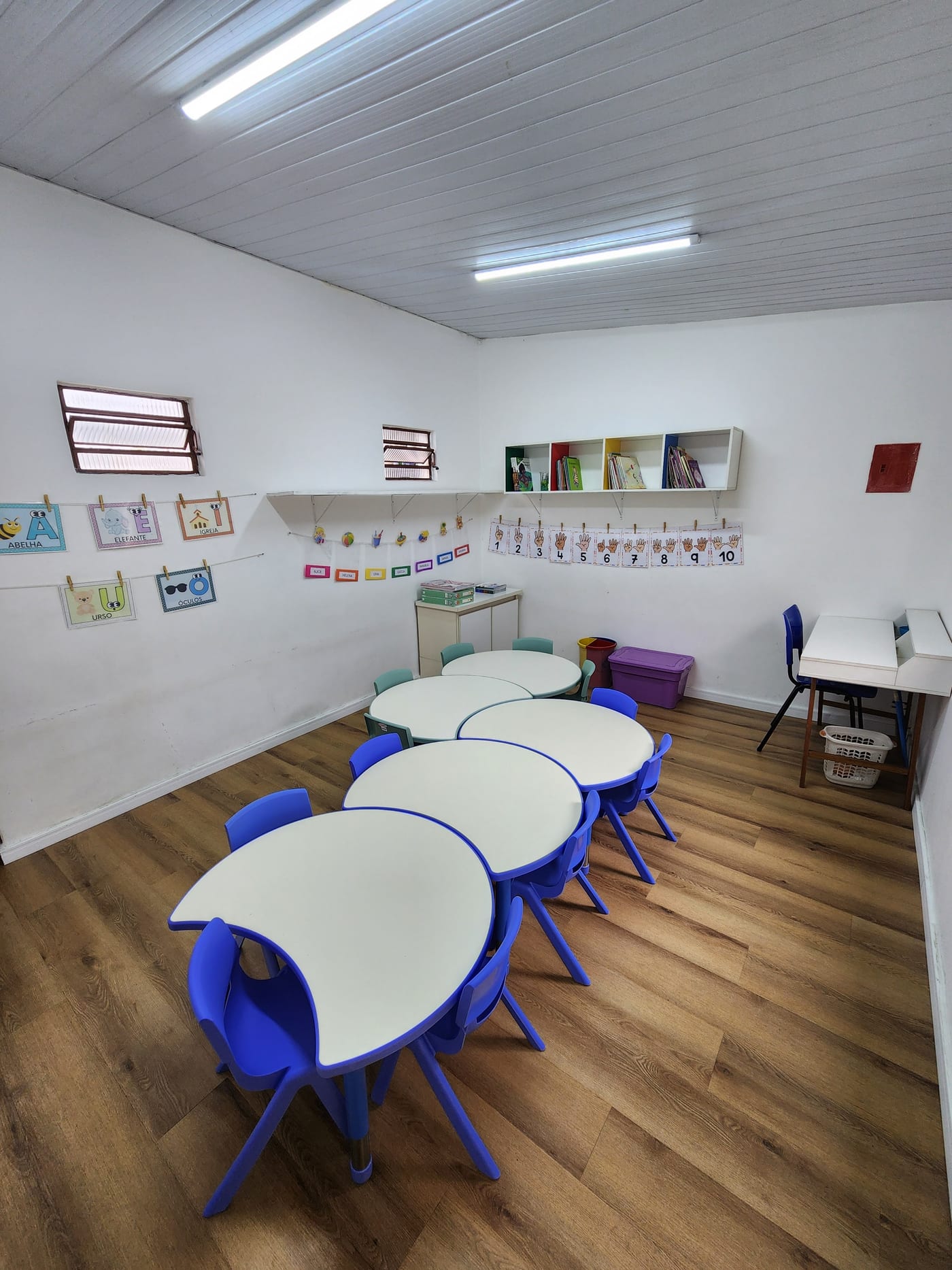 Sala de aula com mesas e cadeiras infantis e trabalhos das crianças nas paredes