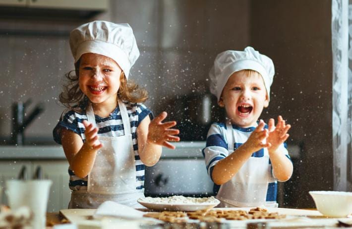 Duas crianças sorrindo com gorro e avental de cozinheiro em uma aula de culinária