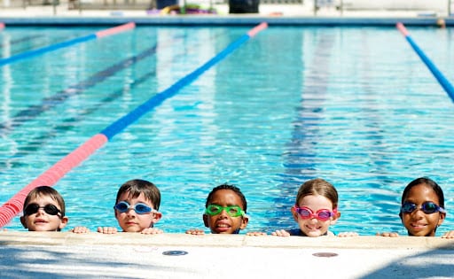Crianças de óculos de natação dentro da piscina, na beira da raia